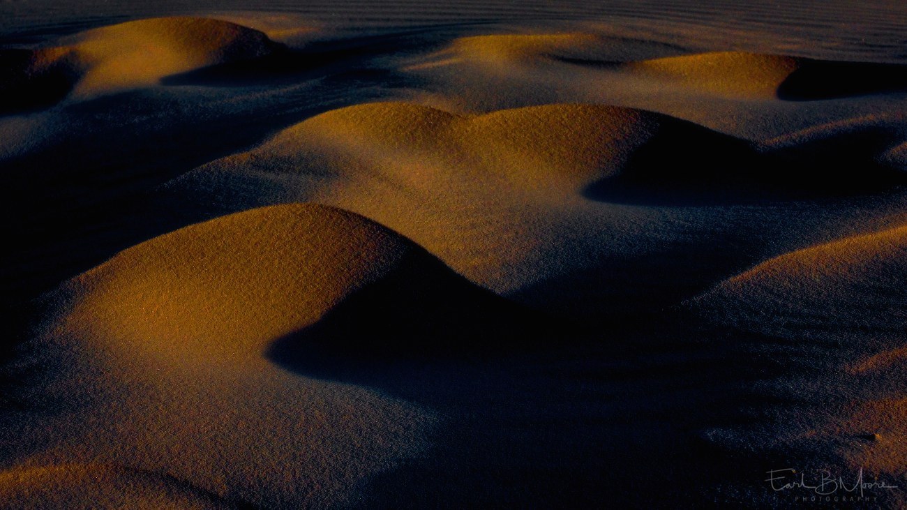 A late evening image with warm tones of mini sand dunes, and deep shadows...wind, sand, and light composition.